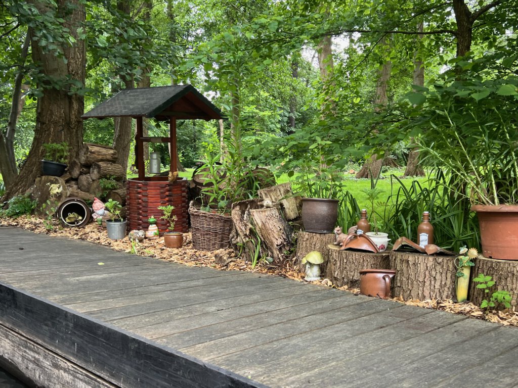 Ein Steg im Spreewald, dekoriert mit einem Brunnen, Baumstämmen, Vasen und Töpfen.