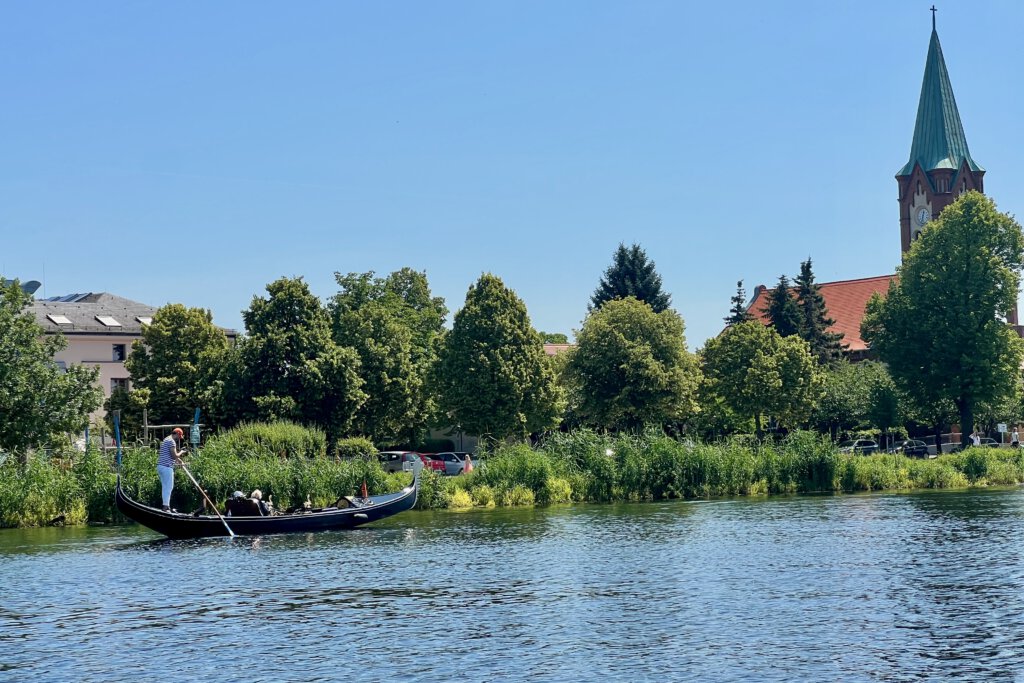 Eine Gondel fährt über die Föhse in Werder (Havel). In Hintergrund siehst du die katholische Kirche