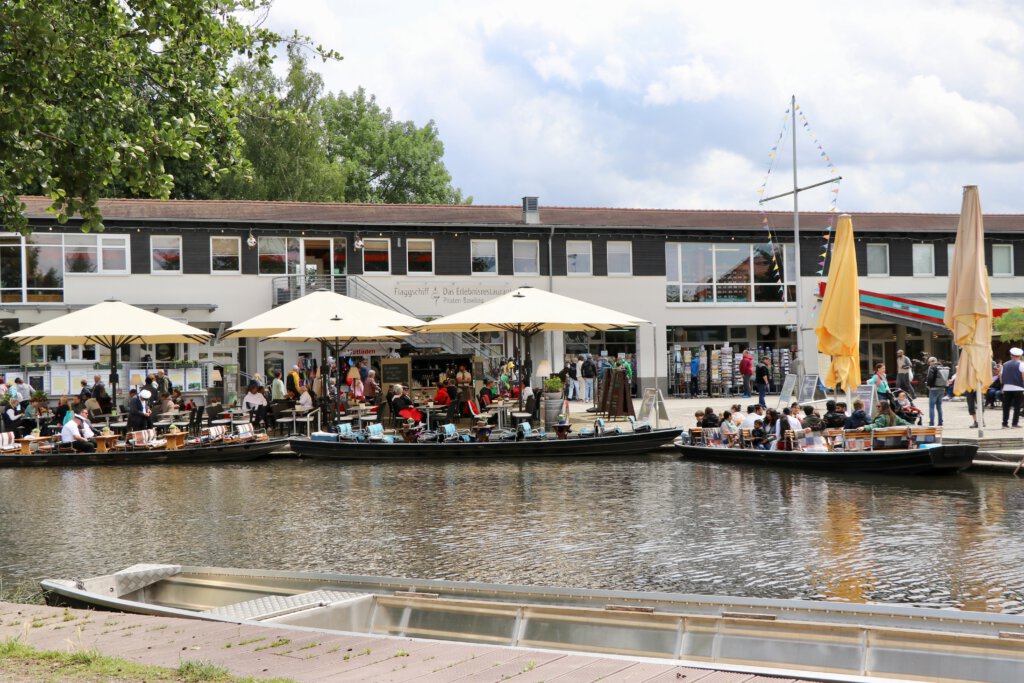 Blick auf den Hafen von Lübbenau. Du siehst die Spreewaldkähne, dahinter ein langes Gebäude mit Geschäften und Restaurants