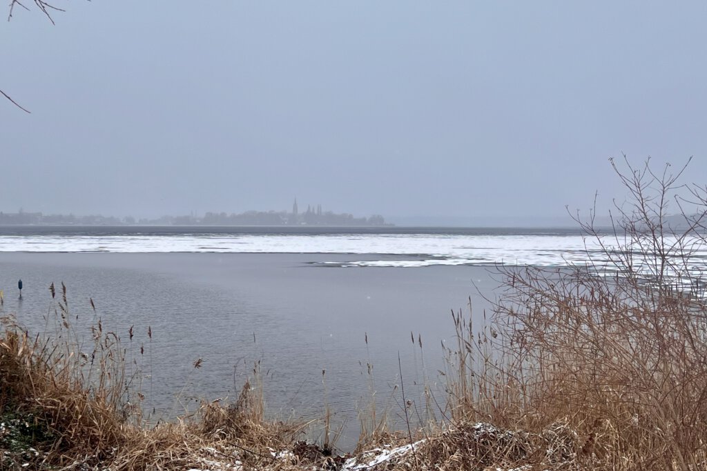 Die Havel ist mit Eis und Schnee bedeckt. Am Horizont sieht man unter dem Nebel den Turm der evangelischen Kirche